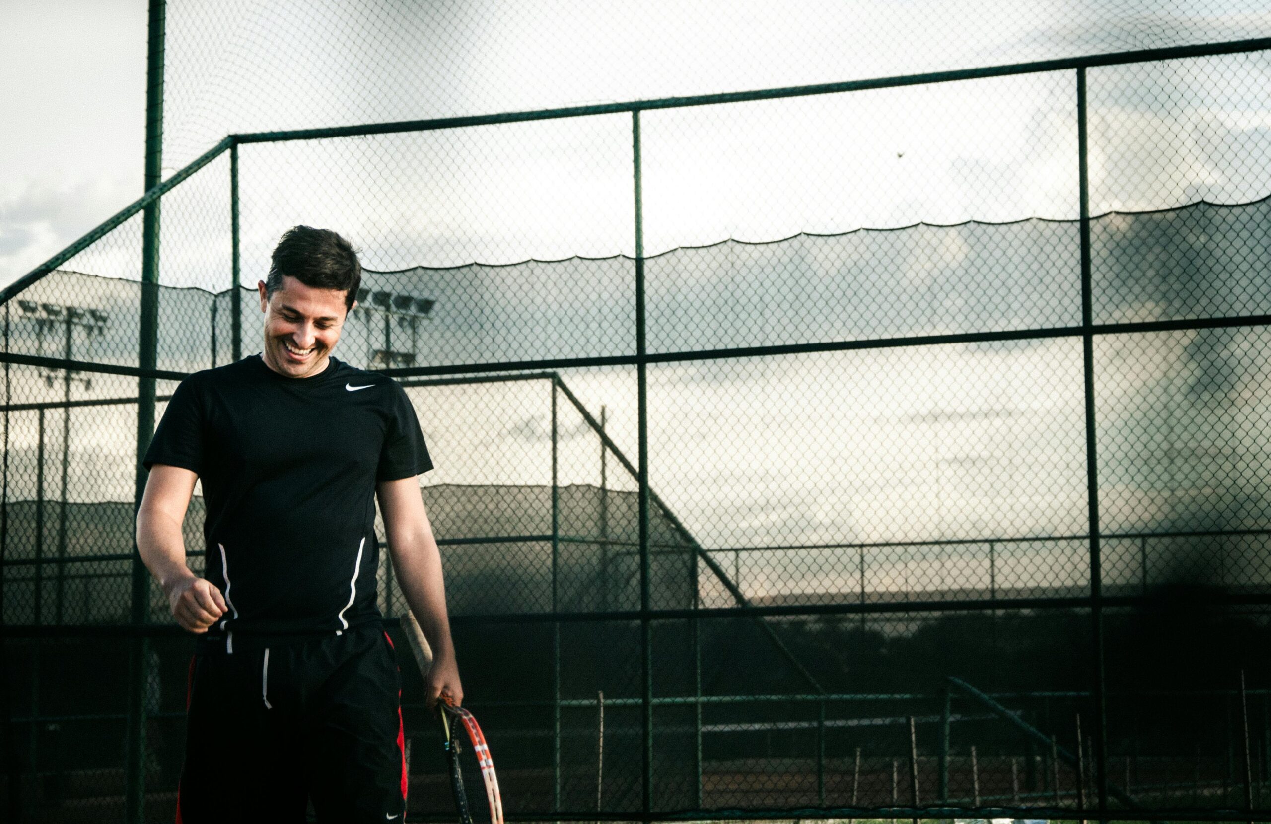 A happy tennis player smiles while holding a racket on an outdoor court.